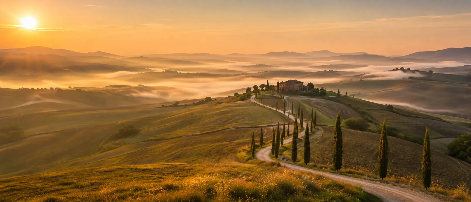 Sunrise over the Val d'Orcia, mist lying in the folds of the hills and a farmhouse on a rise with a cypress-lined track climbing to it